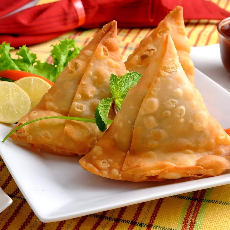 Golden-brown samosas garnished with mint, lemon slices, and lettuce on a white plate.