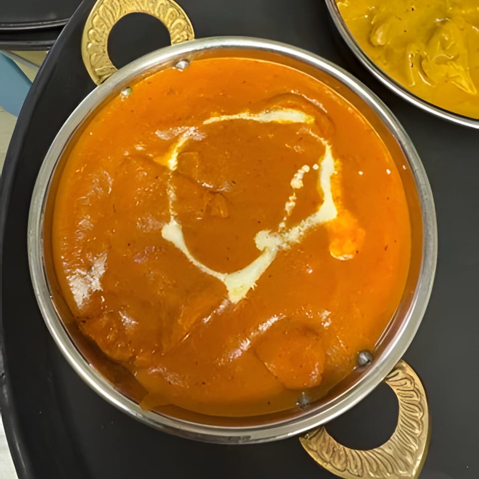 A close-up of Royal India Palace's vibrant orange Indian curry, garnished with a swirl of cream.