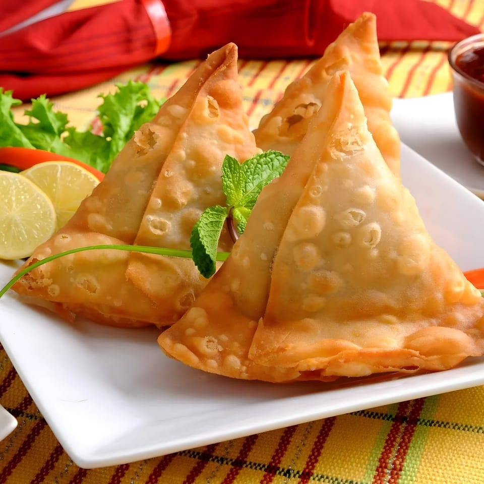 Golden-fried samosas garnished with mint, lemon, and lettuce, served with chutney.