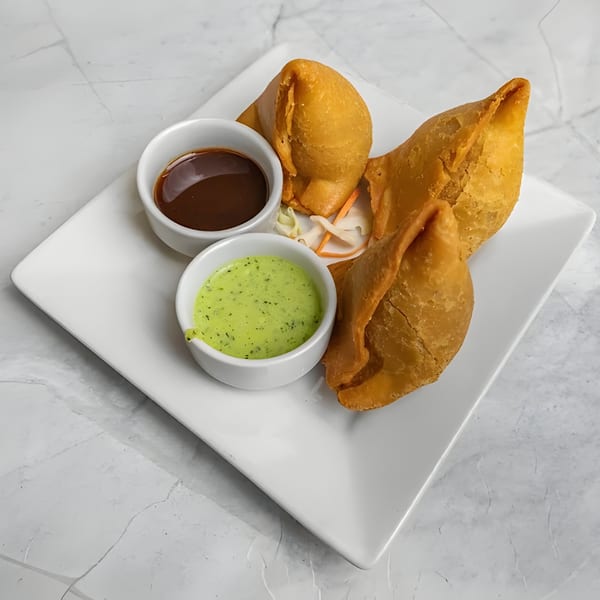Three golden-brown samosas with two dipping sauces, one green and one brown, on a white plate.