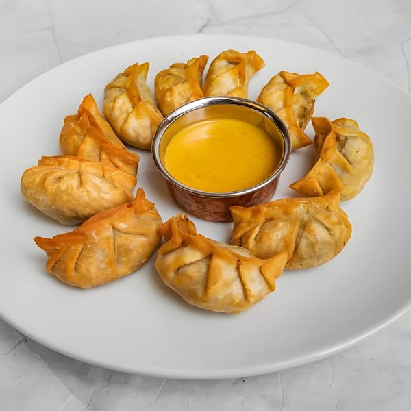 Golden-fried Indian momos arranged in a circle around a small bowl of yellow dipping sauce.