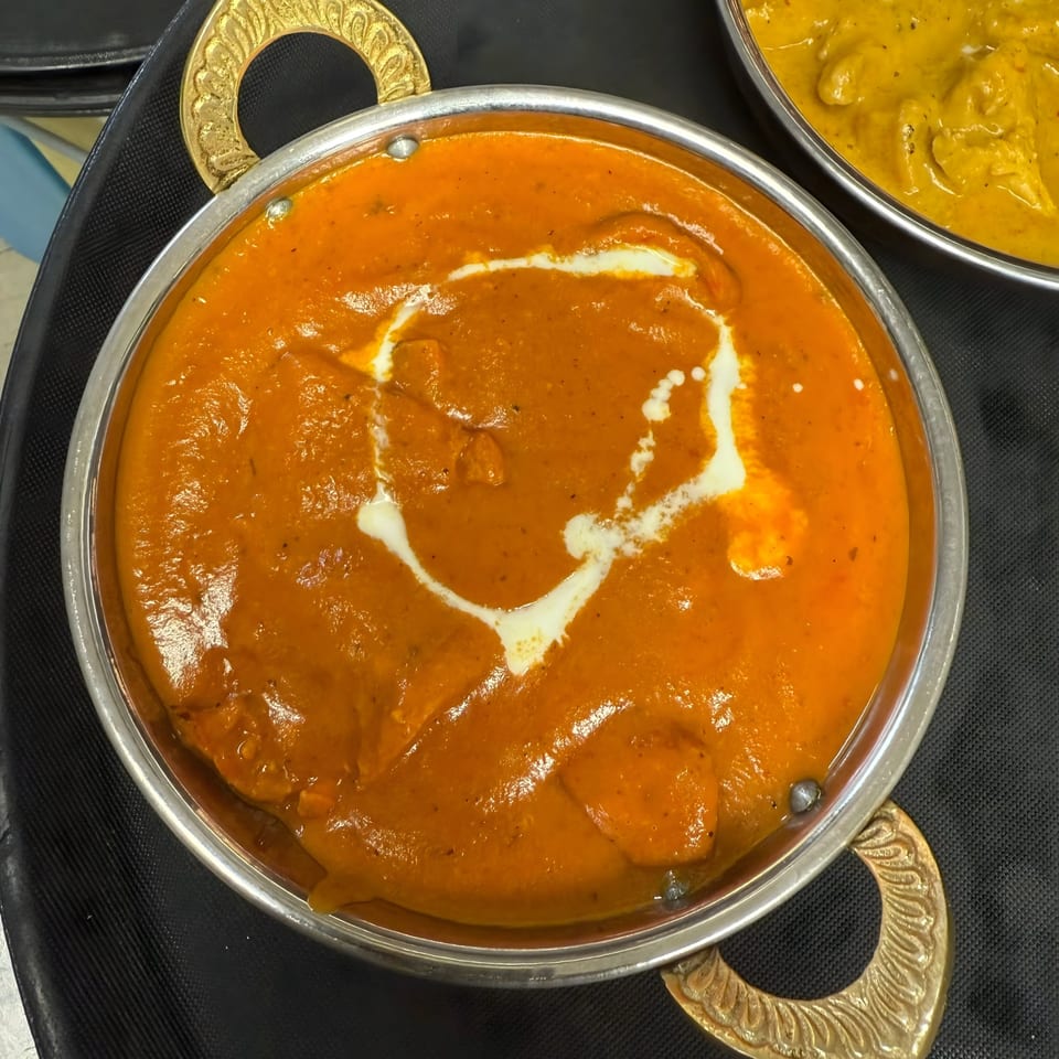 Royal India Palace's butter chicken, a rich orange curry with a swirl of cream in a metal bowl.